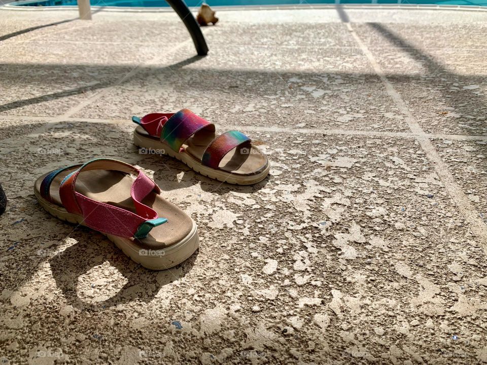 Welcoming Ground Showing A Pair Of Colorful Sandal Shoes On Concrete With Early Day Morning Sun With Lights And Shadows By A Table And A Pool.