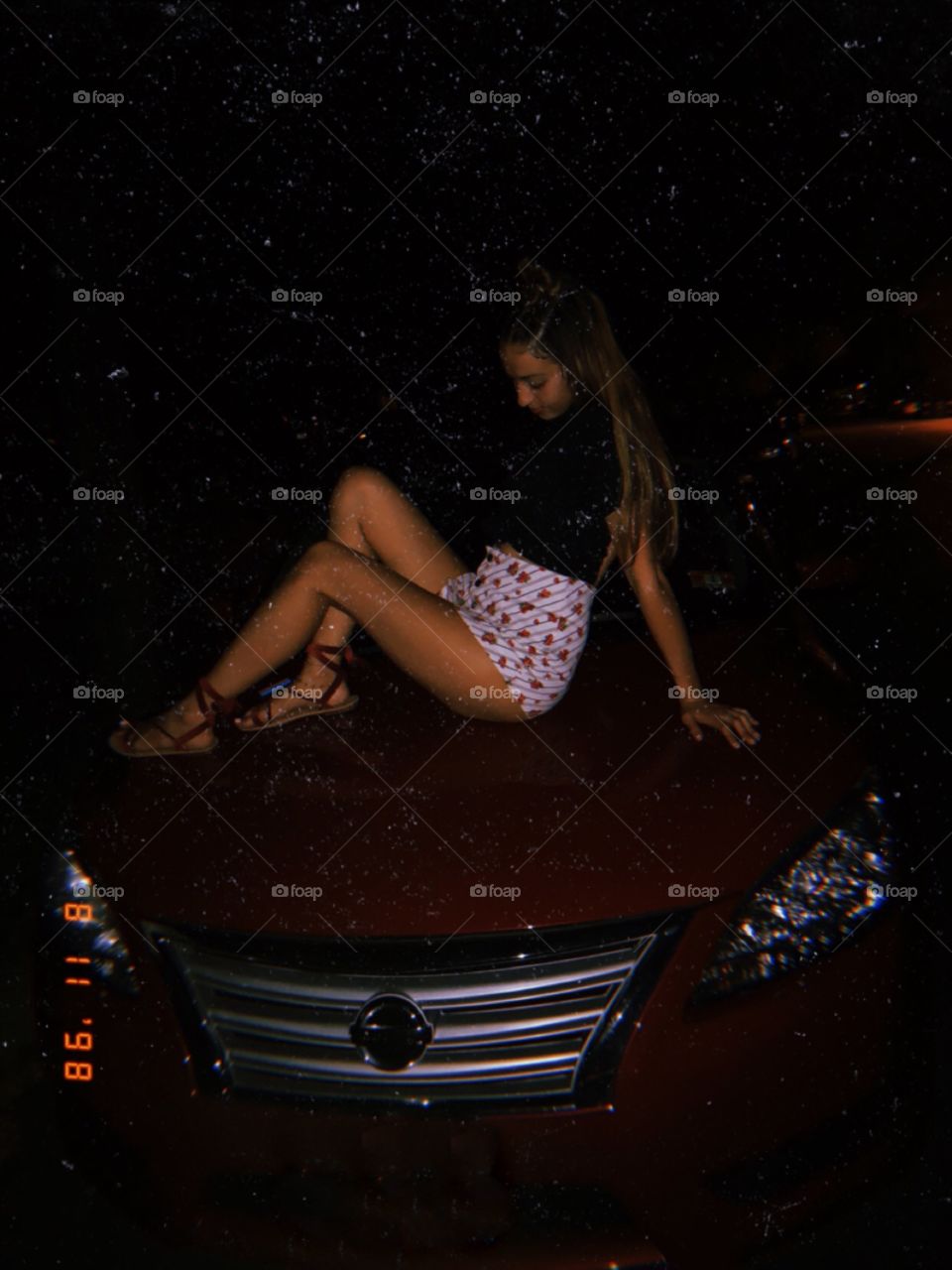 Female sitting on hood of red car at night