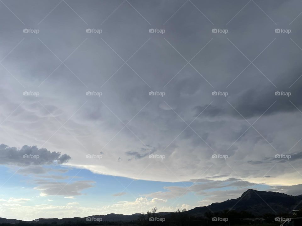A partially cloudy sky with mountains and trees.  