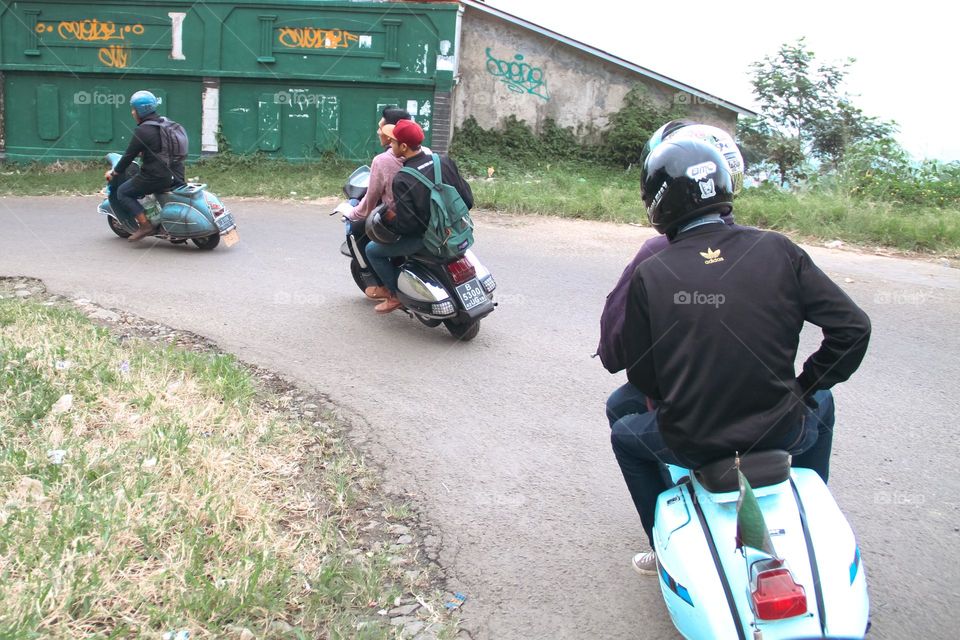 View of three classic vespas on a road walking together.