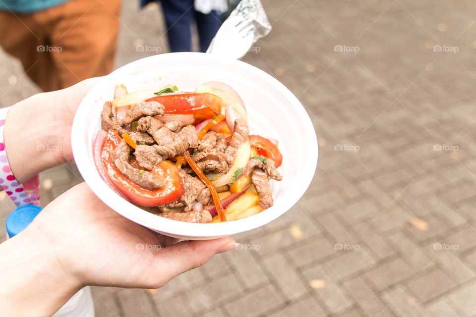 woman holding Lomo Saltado(Perivian food)at street