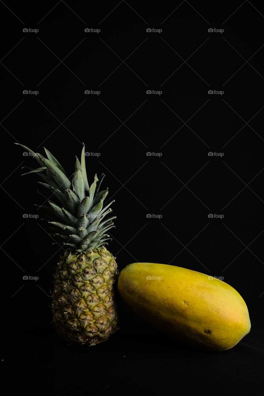 Pineapple and papaya on black background