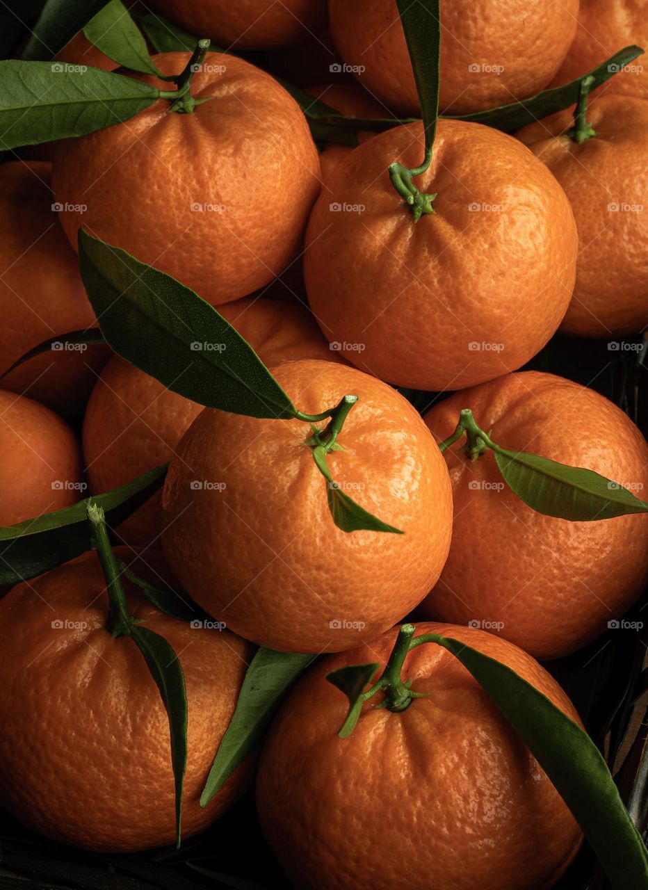 A stack of the clementines with green leaves, fresh from the tree