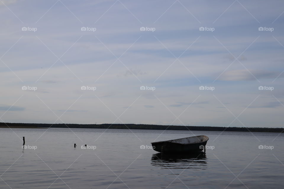 lonely fishing boat docked in calm lake. wooden fishing boat in a still lake water. image of wooden fishing boat moored on the shore. space for text. Toksovo, lake Kavgolovo