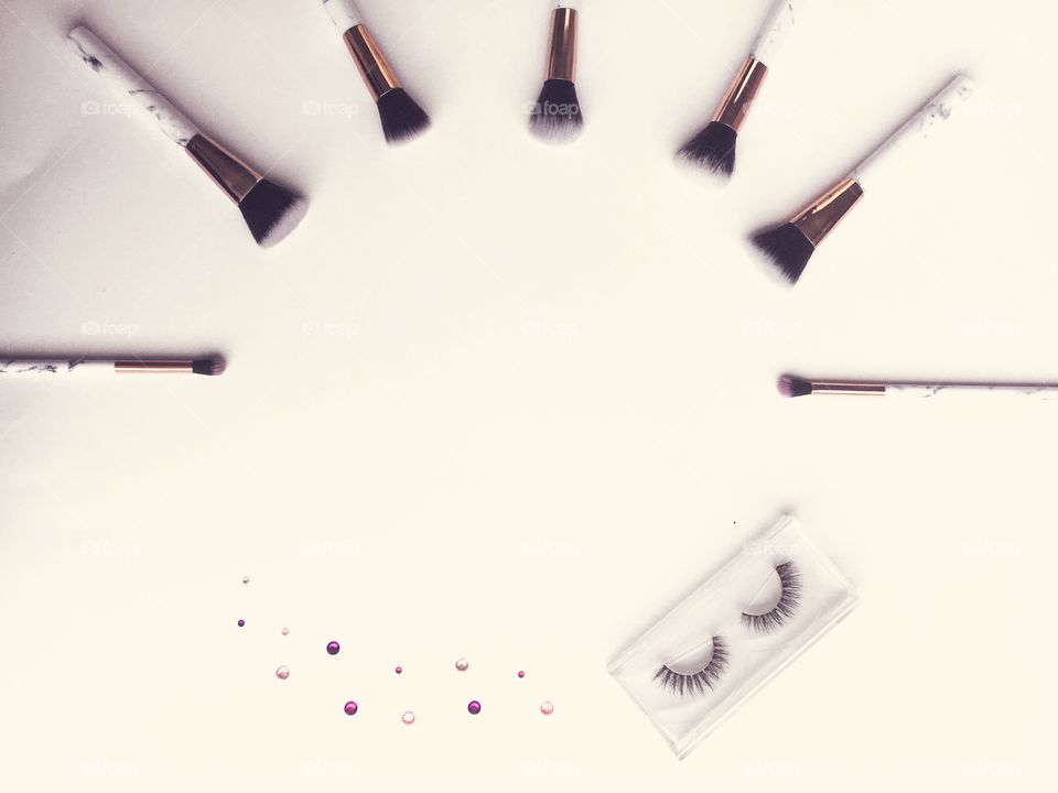 Makeup brushes flat lay with false lashes and a little bit of bling. White background. Edited to a pastel finish.