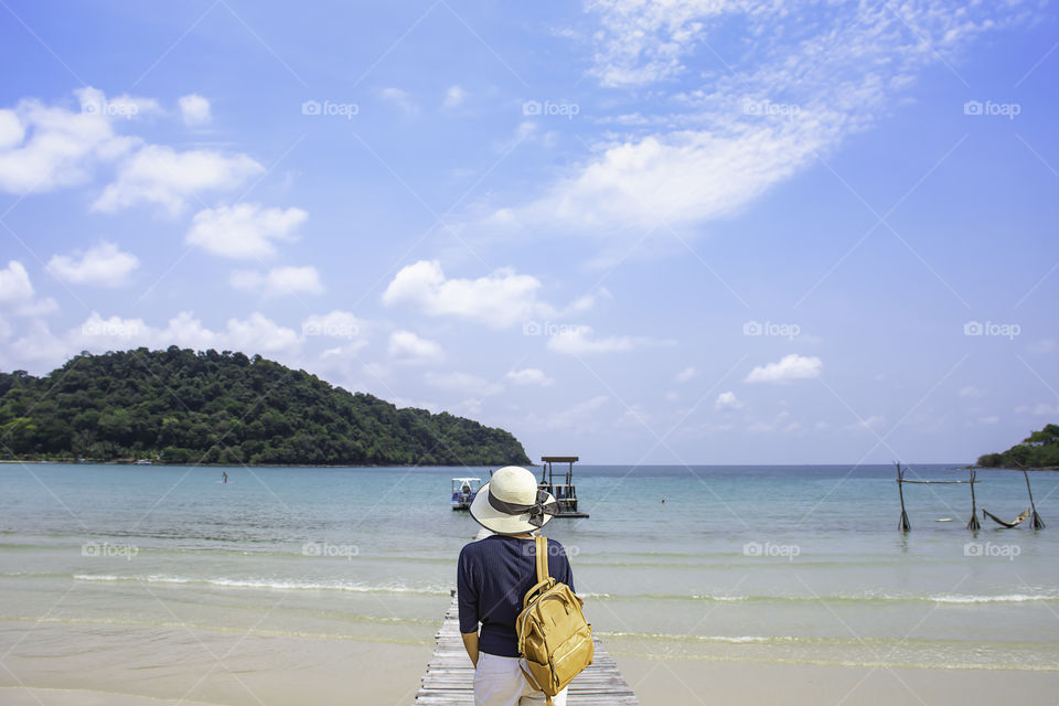 Women shoulder backpack and Wear a hat on wooden bridge pier boat in the sea and the bright sky at Koh Kood, Trat in Thailand.