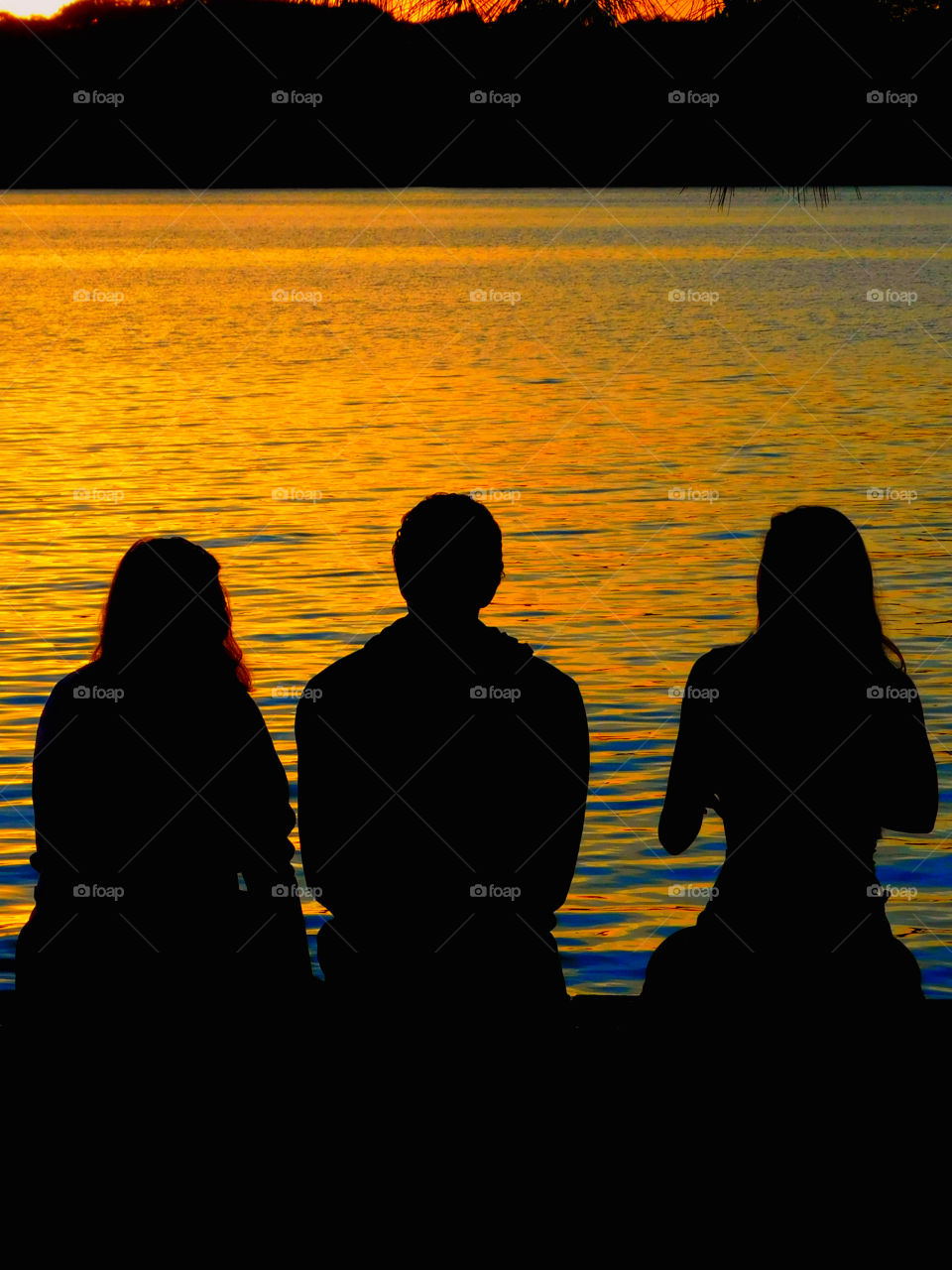 Sitting on the dock of the bay, watching the tide roll away!
Three people sit,talk and bask in the radiant sunset!