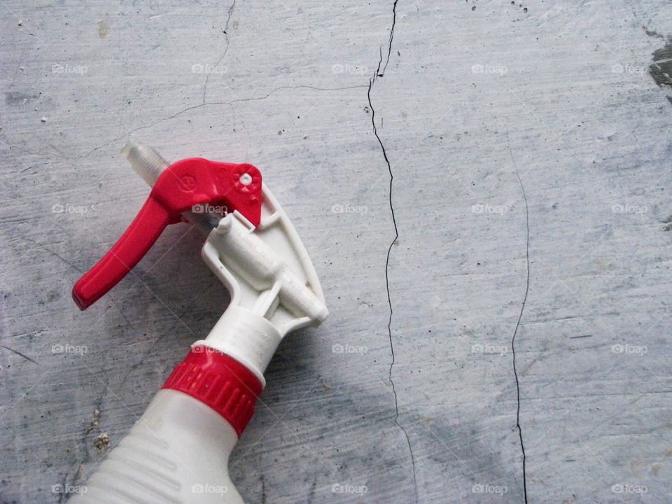 Close-up view of a white plastic spray bottle with a red handle on a cracked gray surface