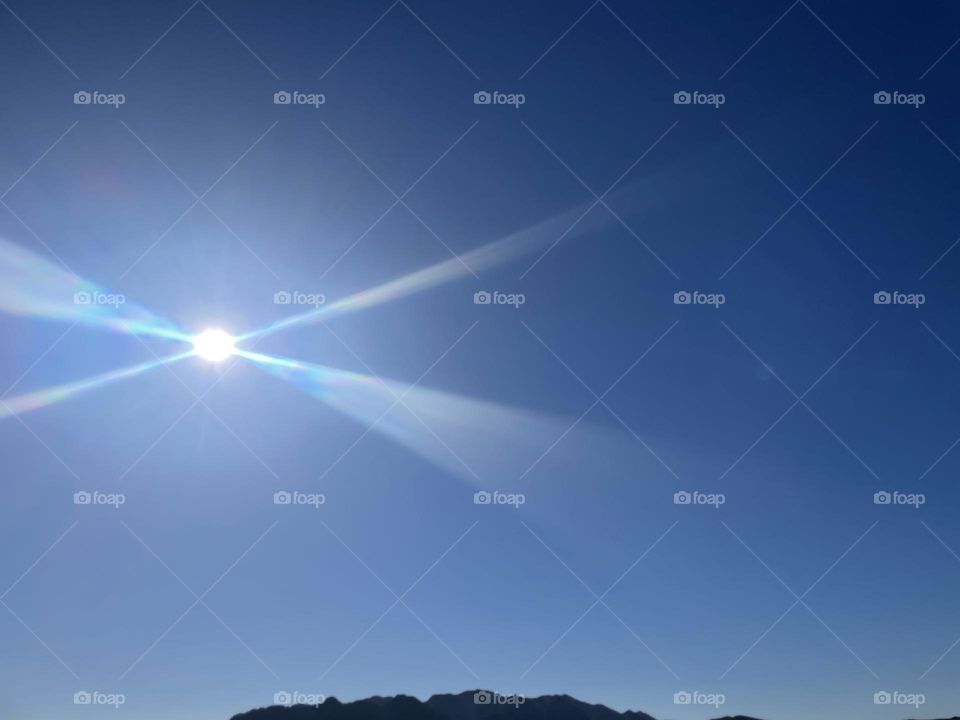 The sun with its rays across the sky and mountains below the sun. 