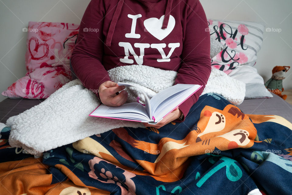 A young girl is reading a book in bed wrapped in a comfortable warm blanket.