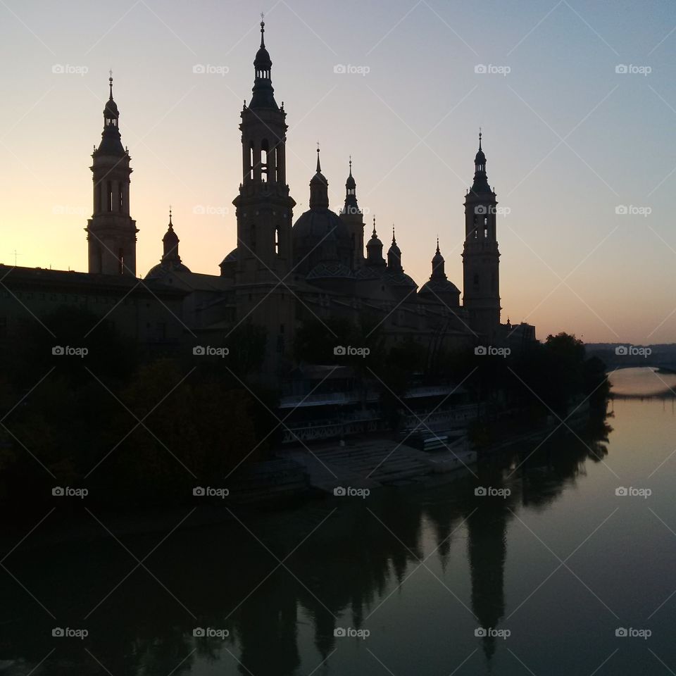 Spires of Zaragoza cathedral reflected in the placid water of the river Ebro below.