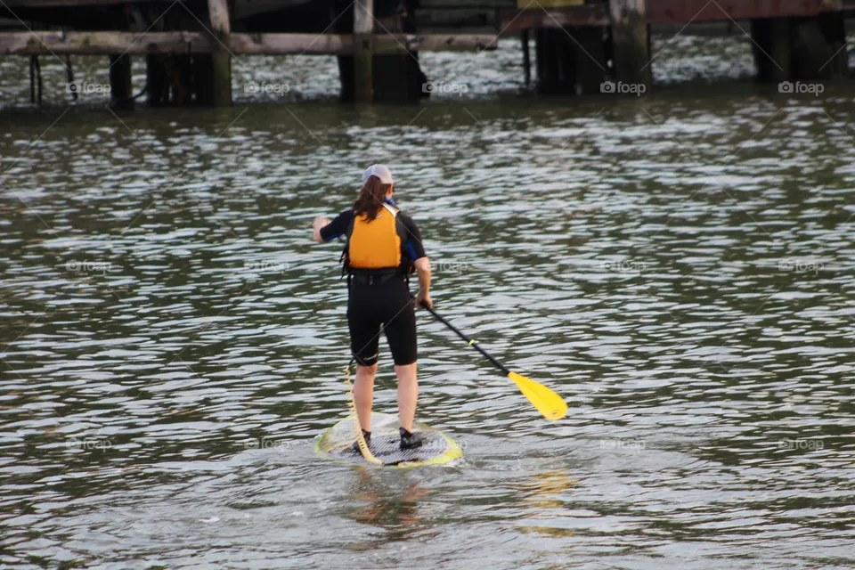 Young woman with orange life vest paddle boarding on Hudson River 