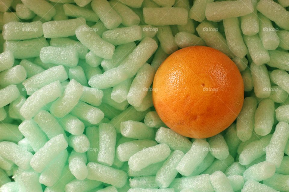 An orange grapefruit lies in a box on green packaging chips