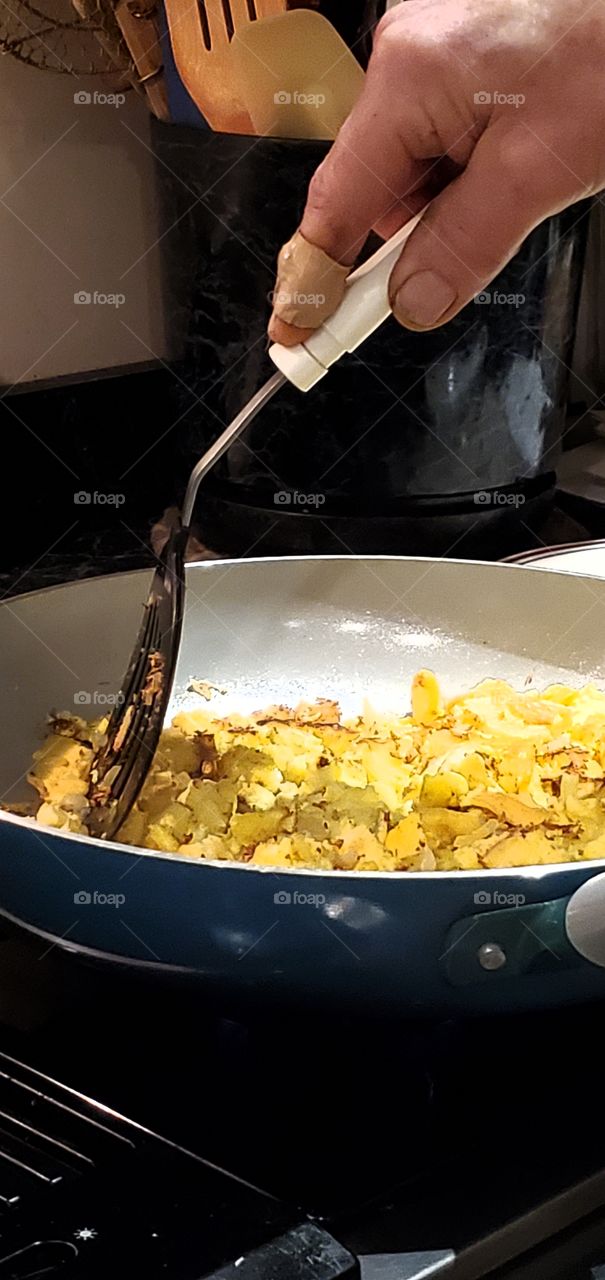 #stayathome - cooking Cook making scrambled eggs in large frying pan. Keeping eggs from sticking by utensil.