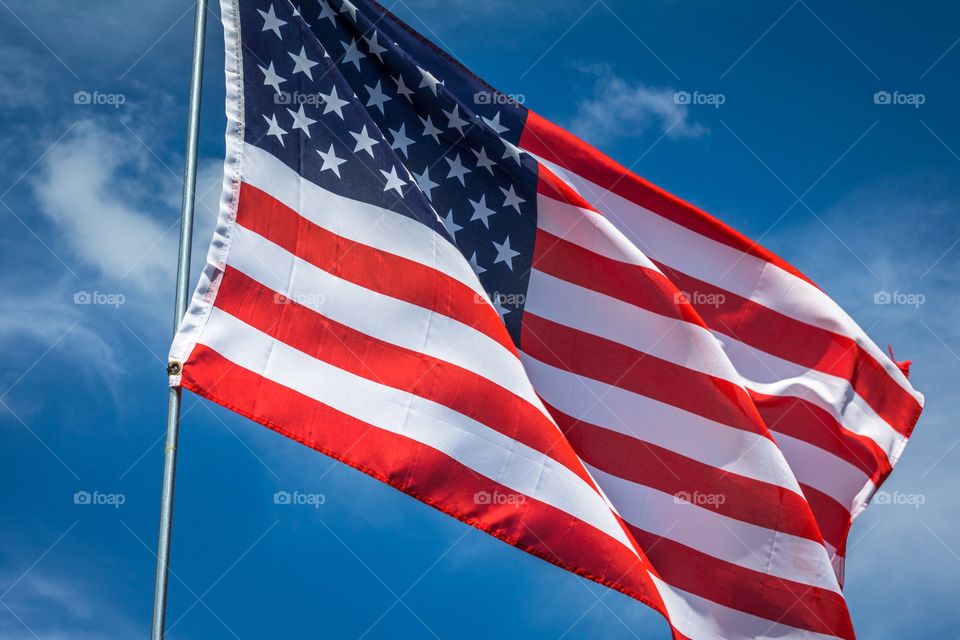 Horizontal photo of a red, white and blue American flag on a silver pole waving in the breeze