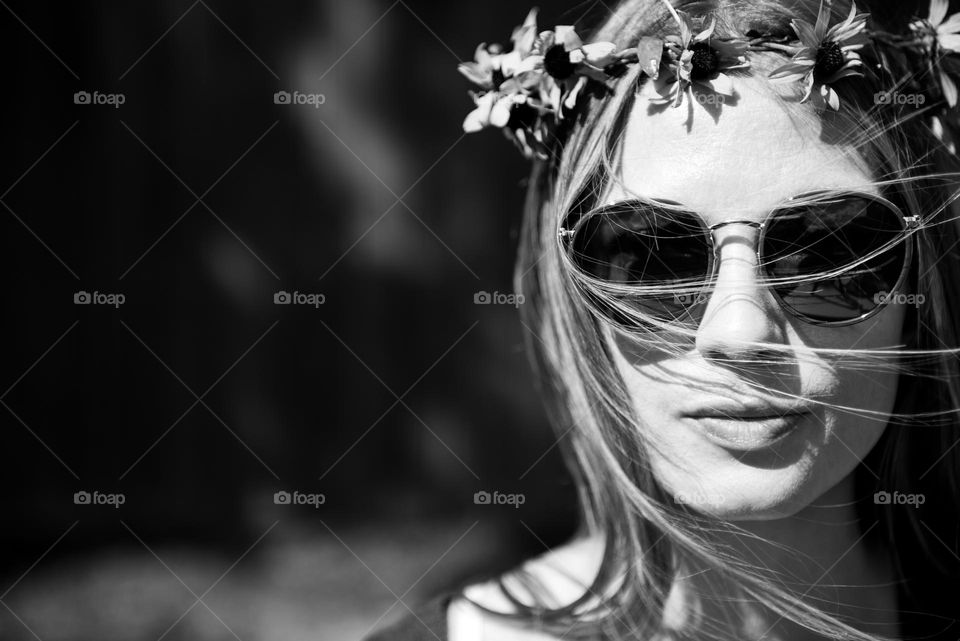 Black and white image of young woman wearing retro sunglasses and a crown of flowers 