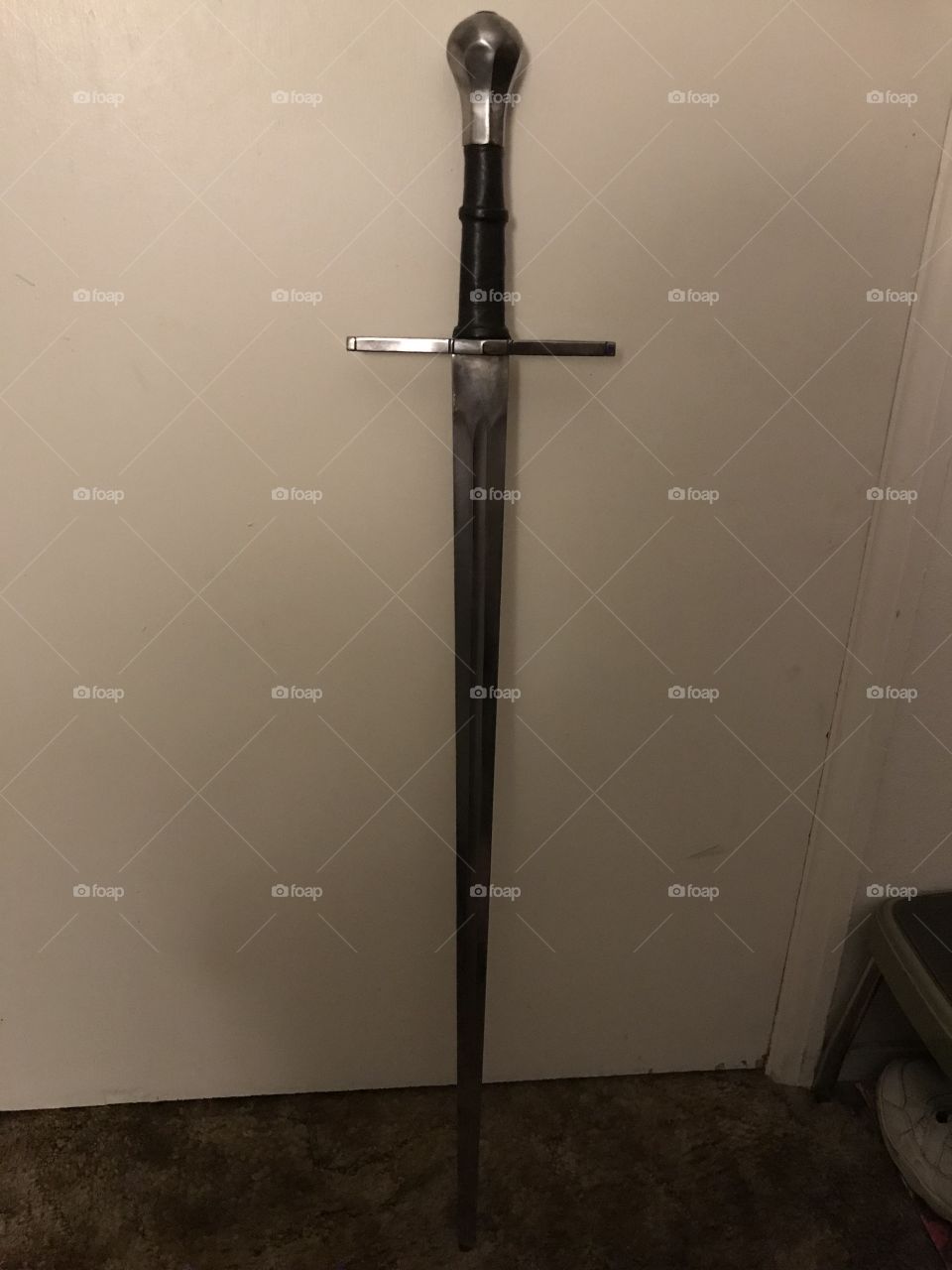 A medieval arming sword that is a marvelous sight for sore eyes. It is leaning on the door waiting to be used by its wielder.