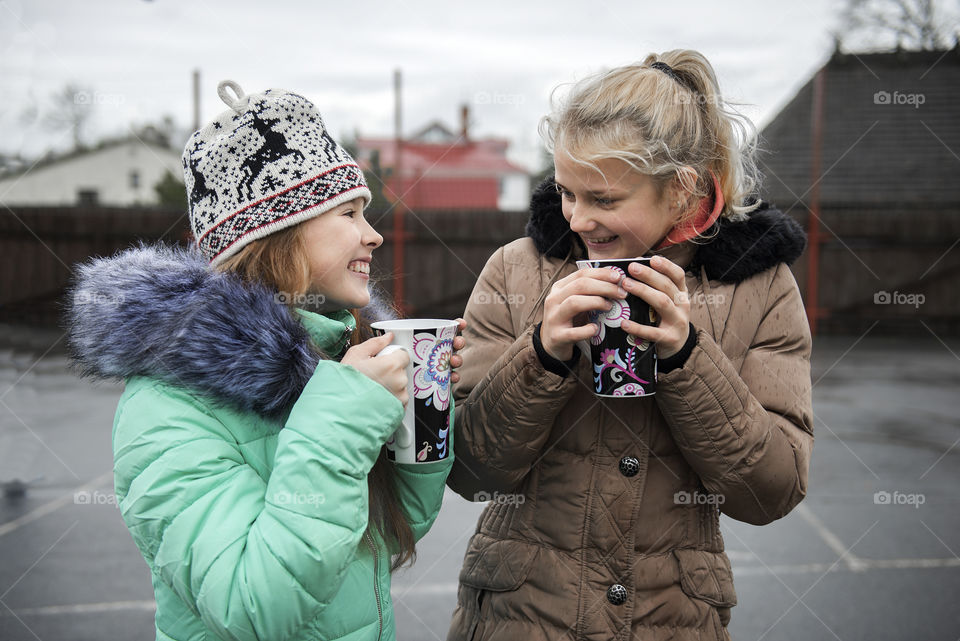 Two teenage girls drink hot tea from big mugs on a cold winter day