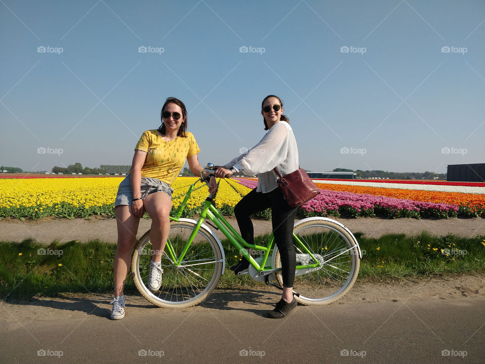 Two girls on a bike in front of a yellow tulips field