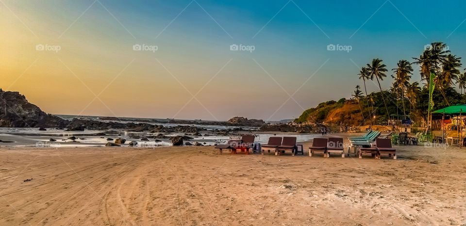 Beauty of Beach - The beach is surrounded by colourful Nature that is sky ,chairs and coconut trees propped on hill.