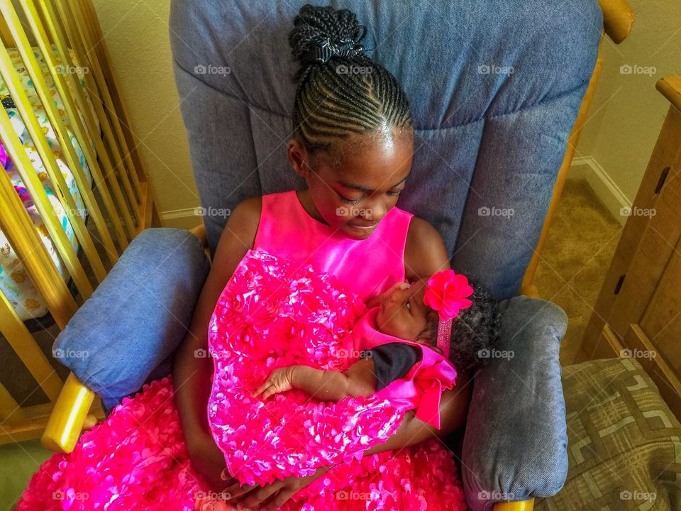 Big sister holding a little sister and they are dress in the same dress