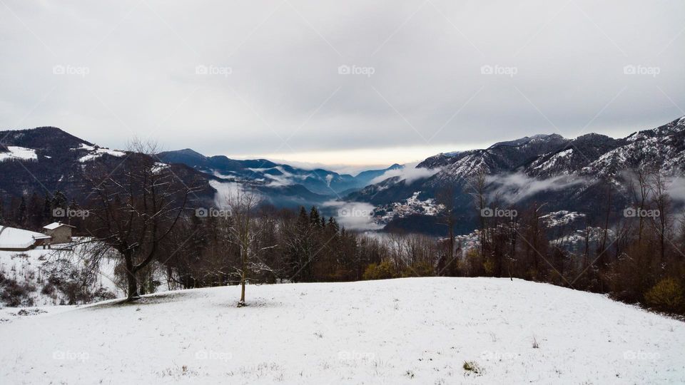 Alpine panorama in January with clouds and snow on the walley in the afternoon. Italian Alps 