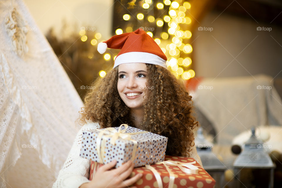 Pretty lady woman laying on Christmas giftboxes wear knitted pollover and santa hat