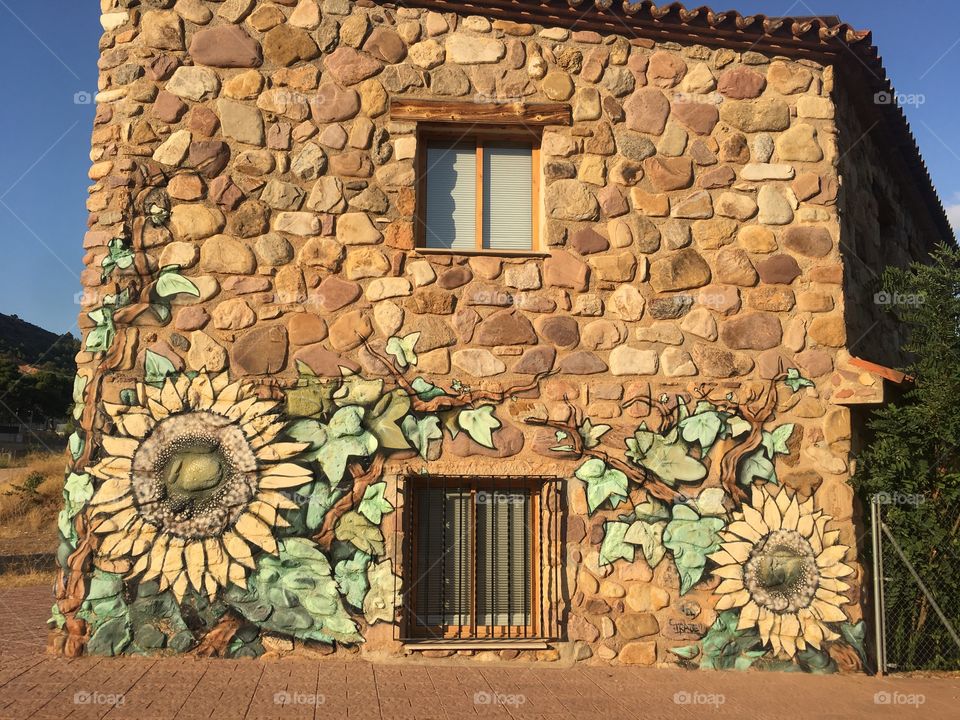Small house made out of colorful stones and decorated with a mural of sunflowers that complemented the colors of the stones.