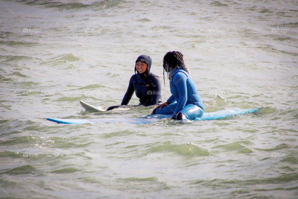 Two women are chatting while on surfboards