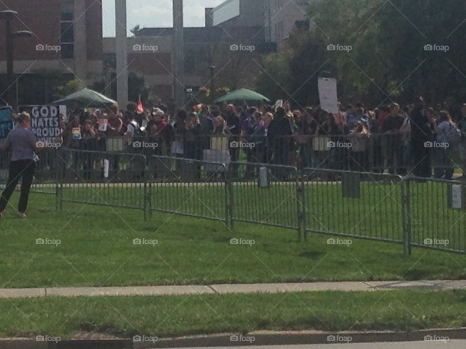 Westboro Baptist church members holding signs to protest an LGB club formed by students of IUPUI.  Club supporters and spectators stand in the background, beyond the fence.