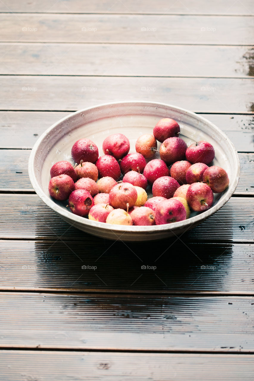 Closeup of big bowl of fresh red apples sprinkled raindrops on wooden table