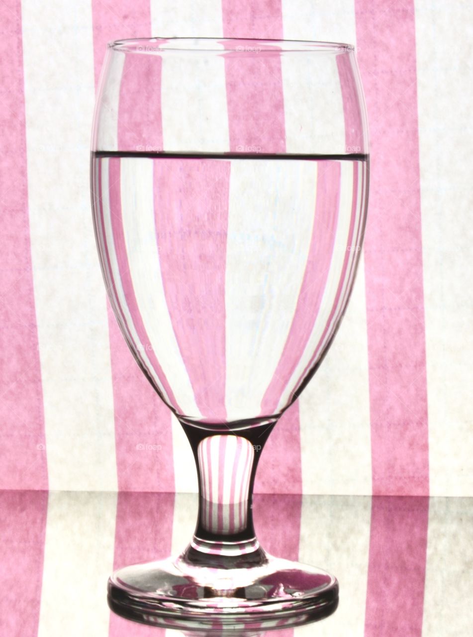 Water in a wine glass refracting water, background pink and white striped 