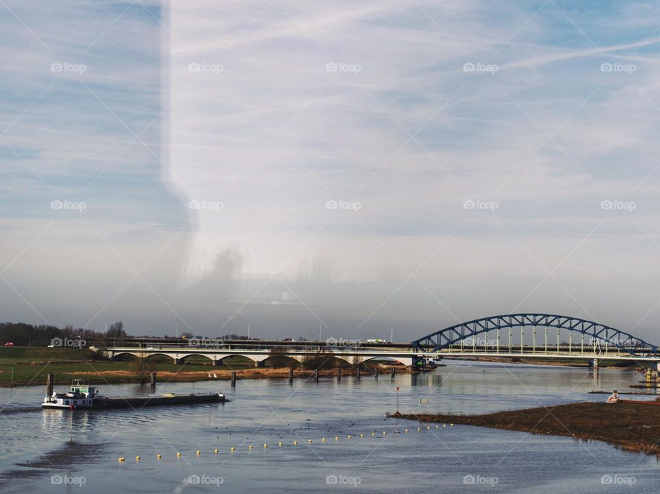 River the Maas in The Netherlands, a cargo ship on the river, bridge. Picture taken from the train