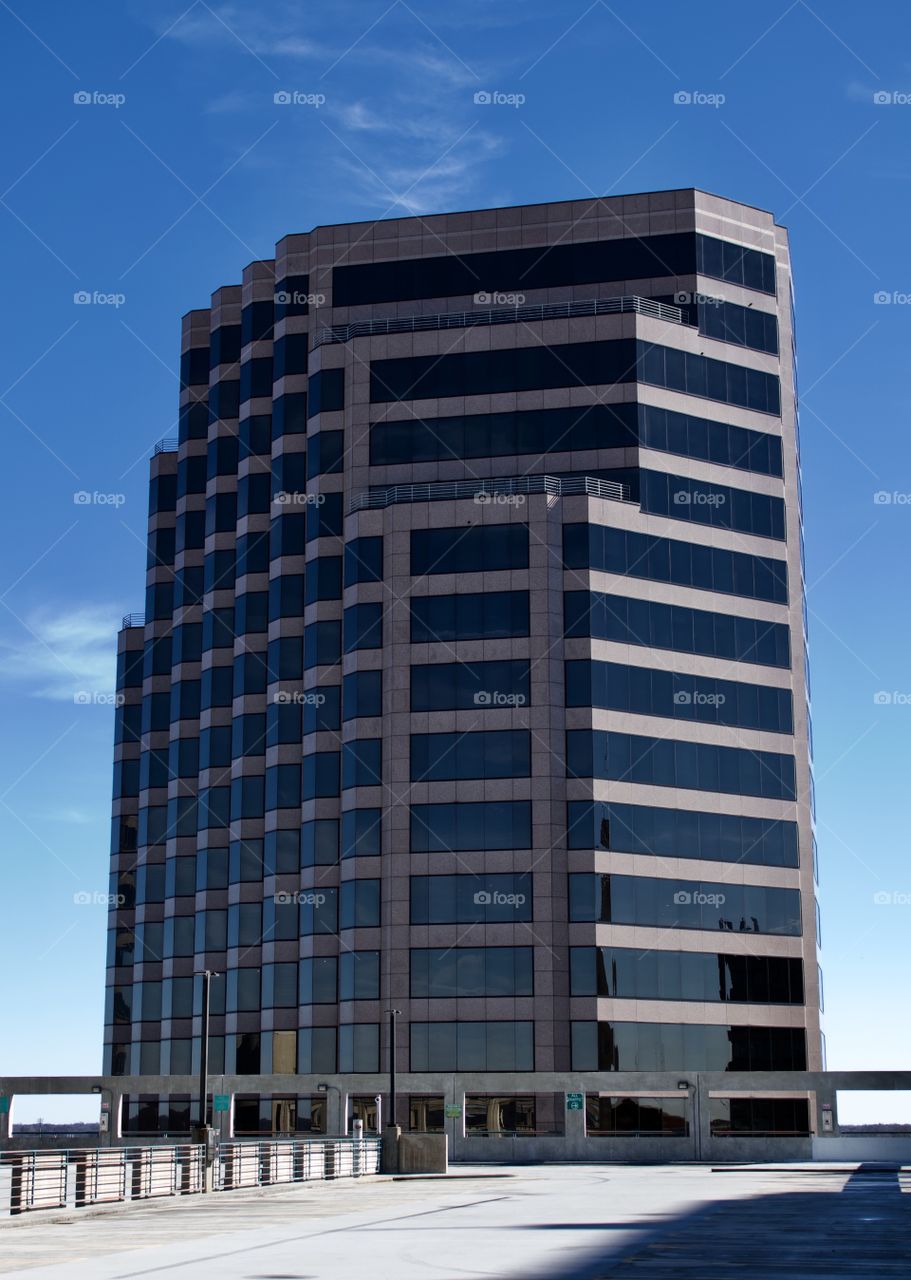 Modern high rise with black glass and marble exterior set amidst blue sky and white clouds.