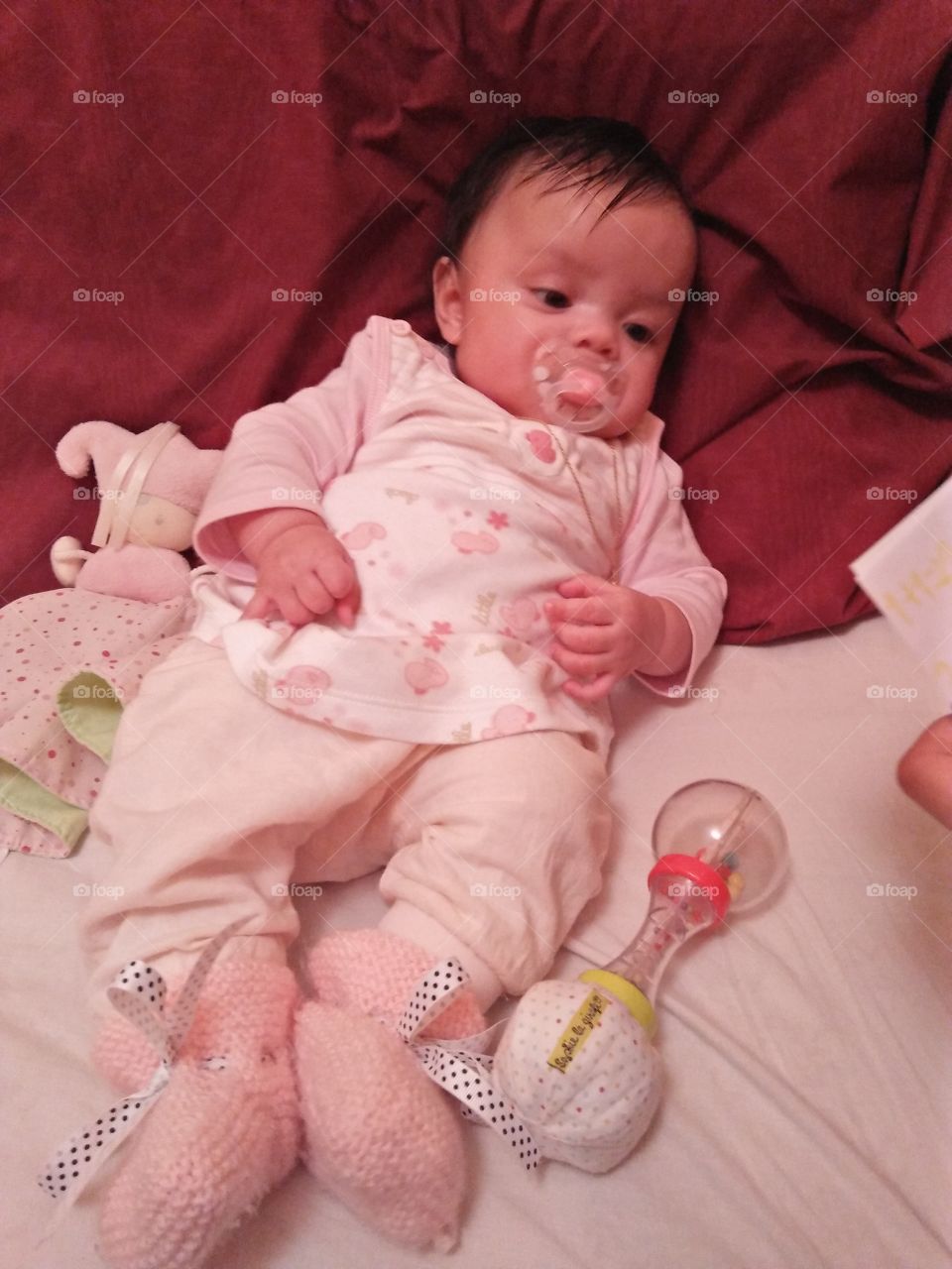 my baby wearing her little duck pink dress design, pink sweater, orange socks while on the bed with her toys.