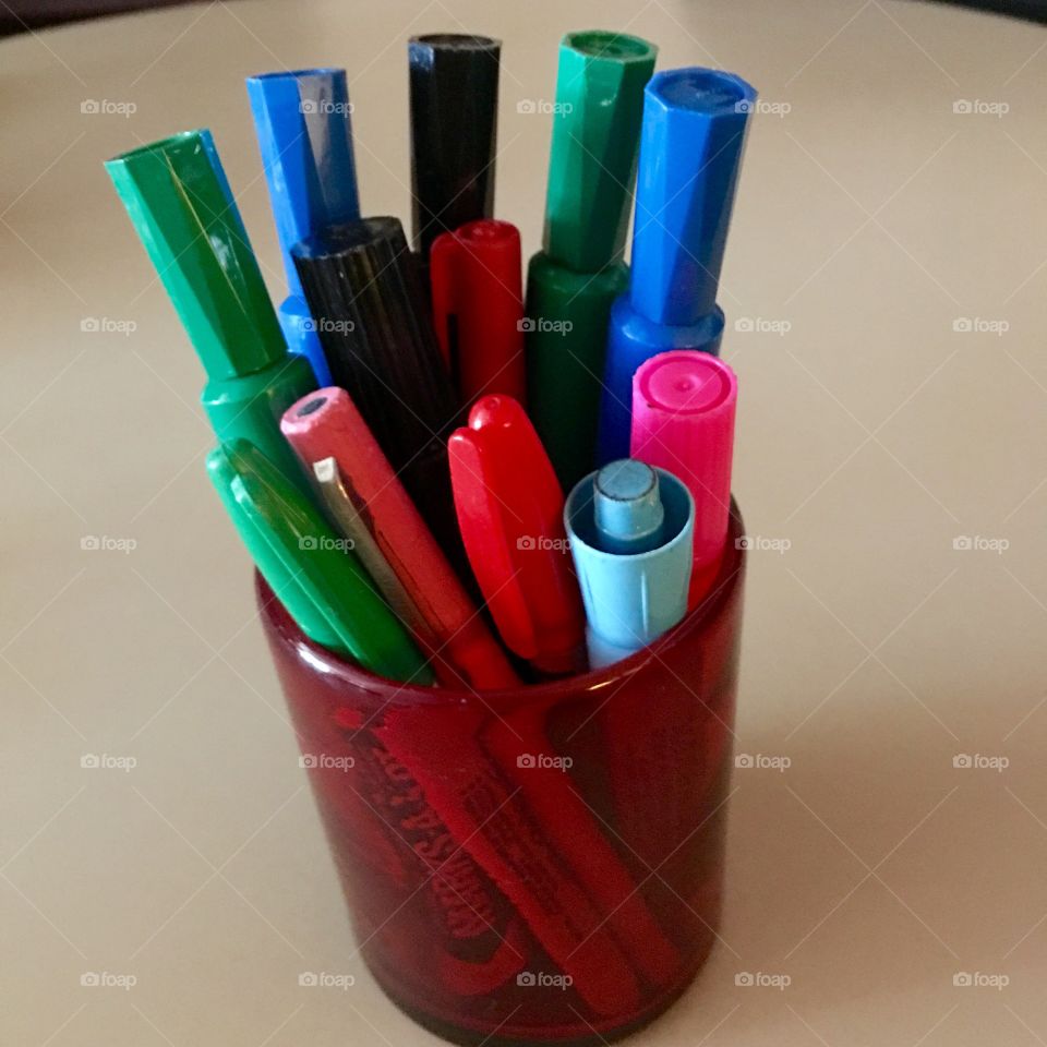 Multi colors permanent markers in red glass holder.