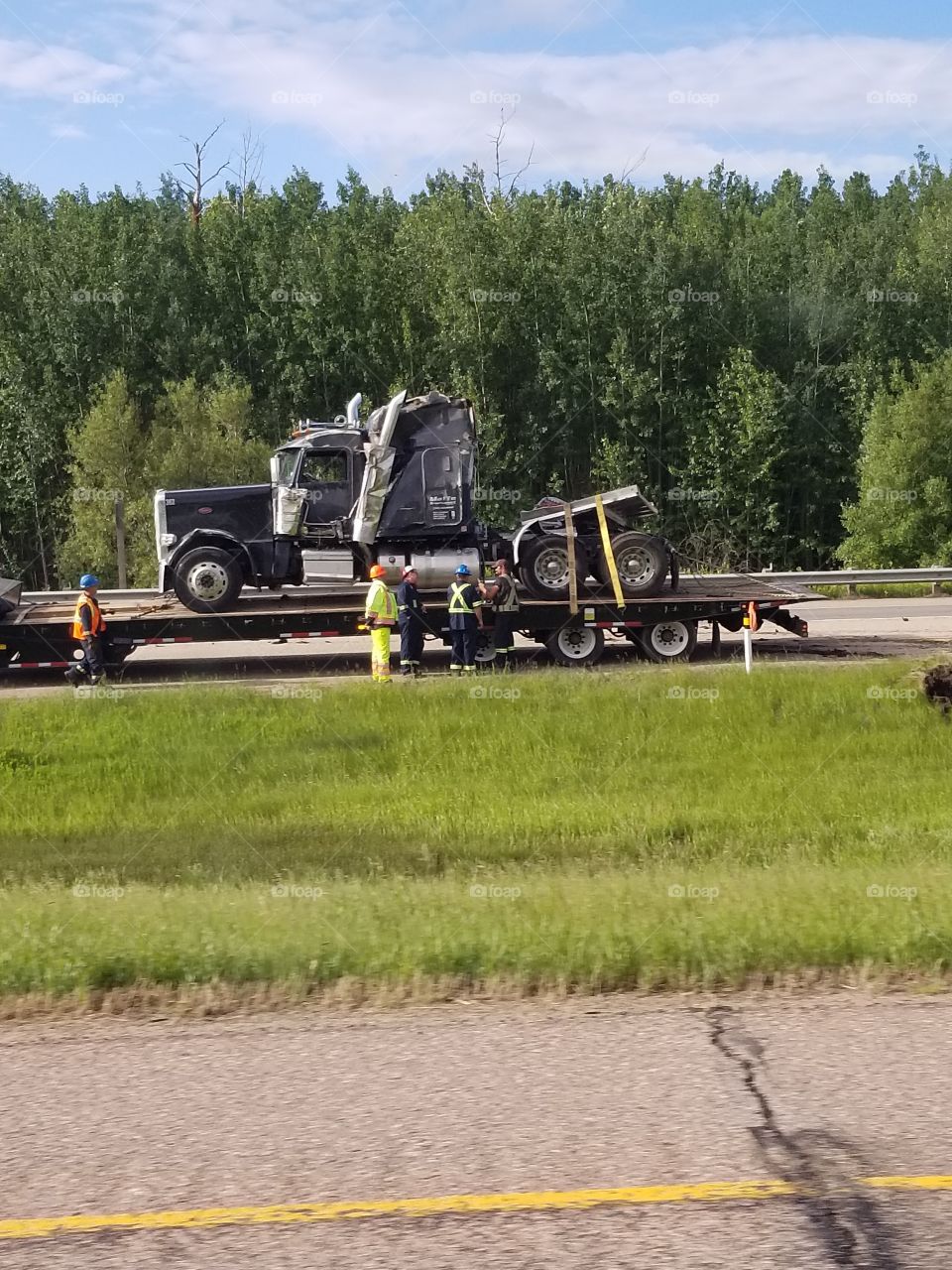 Highway tractor rolled over its load of wood on the highway. The semi truck was loaded onto a flat deck trailer and hauled away.