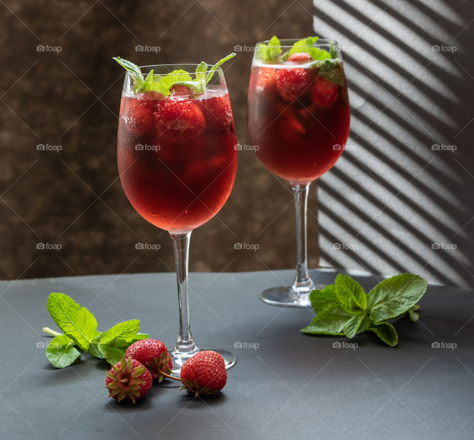 Two glasses with fresh drink with  strawberries, green mint leaves  and ice on the table.