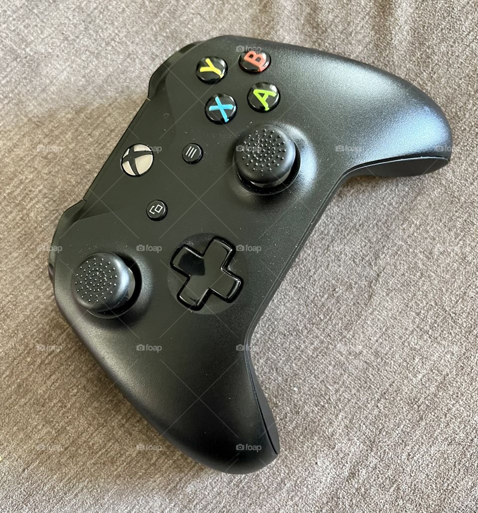Black handheld Xbox video game controller used in a living room at home for entertainment on the tv.  Used for fun on different types of games by pushing buttons and using thumb sticks