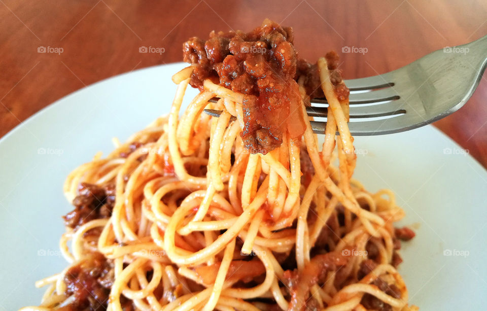 Spaghetti Bolognese with minced beef, onion, chopped tomato, garlic, olive oil, stock cube, tomato puree and Italian herb. Traditional Italian food in white plate with a fork.