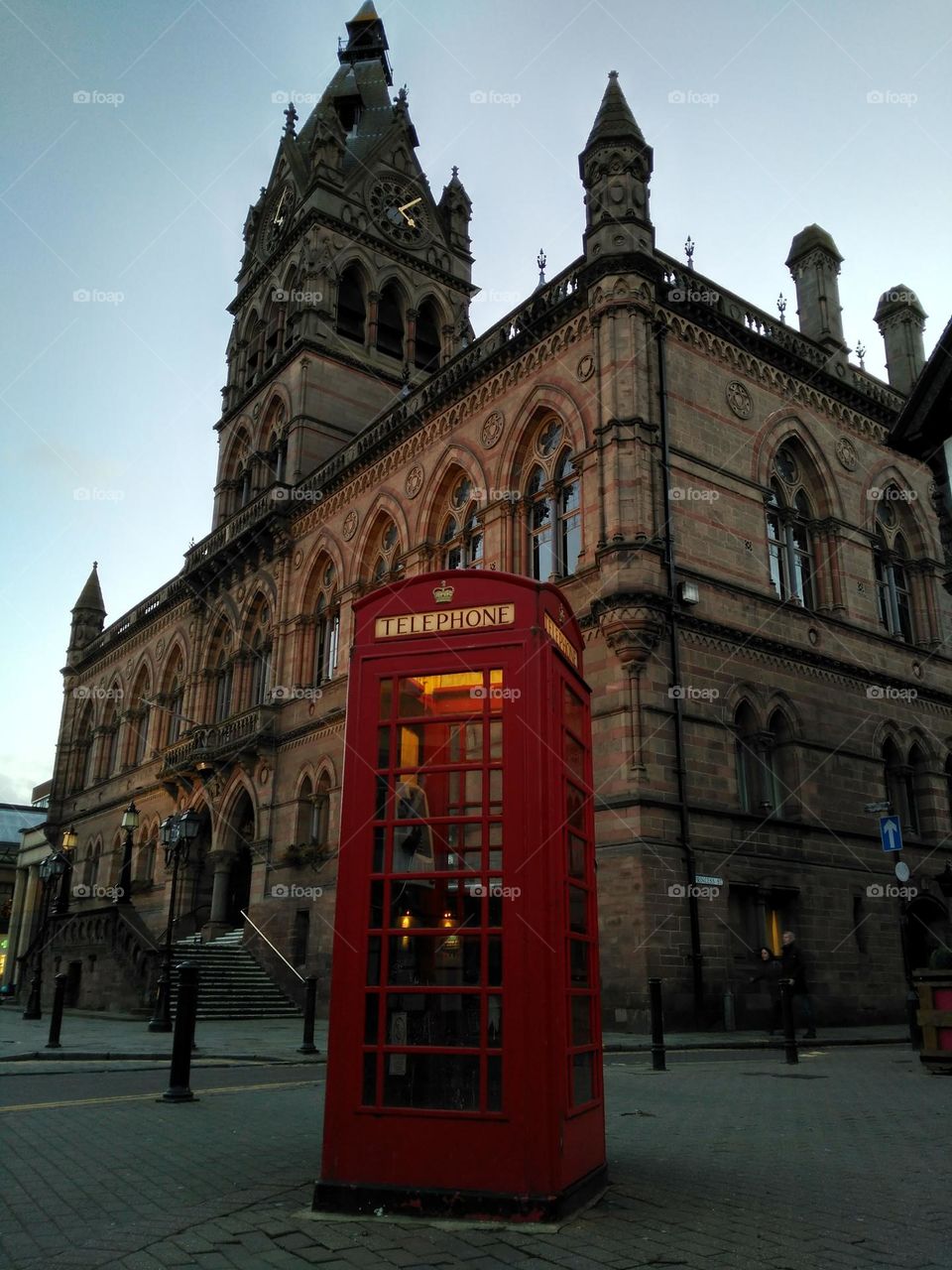 A typical English red telephone booth, in the background an emblematic building of the city of Chester bathed in the evening light on a winter afternoon.