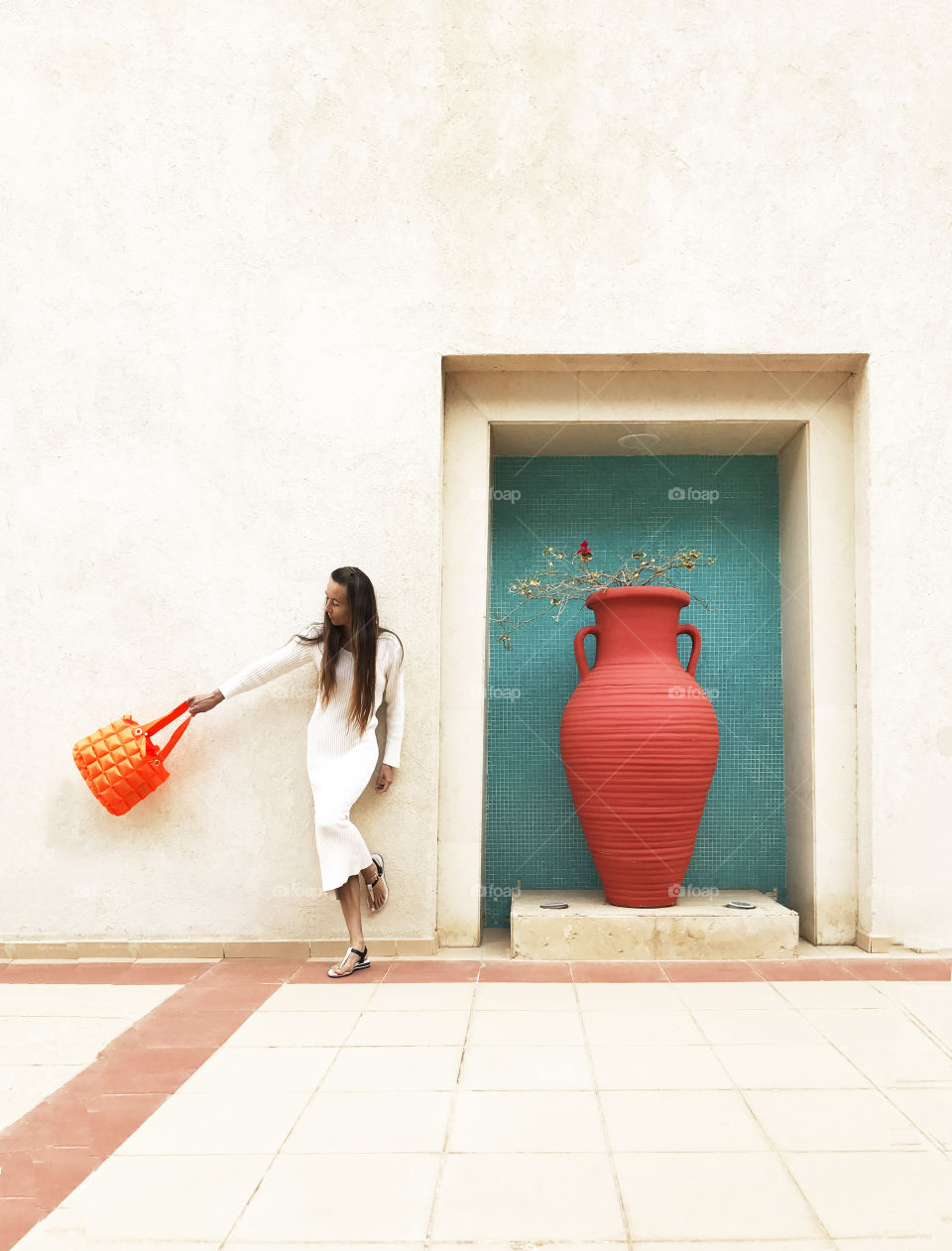 Young woman with orange purse standing nearby huge orange jar 