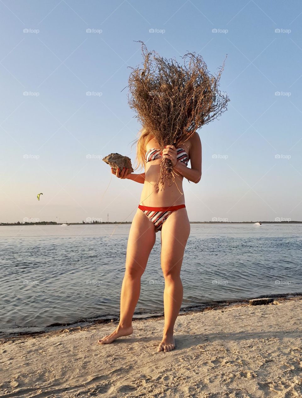 Woman in swimming suit stands alone at the beach with dry flowers bouquet 