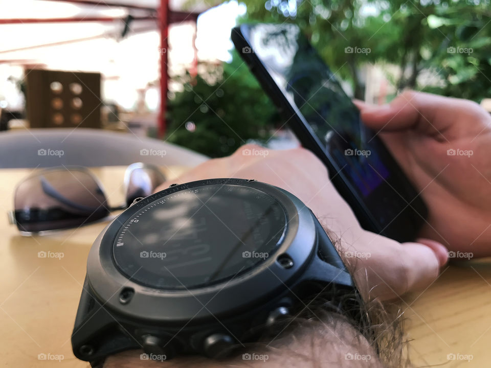 Young man making synchronization of his new smart watches and his favorite smart phone outdoors