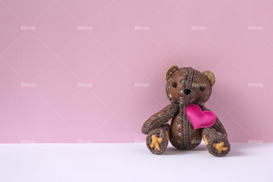 Toy bear with pink heart seats on pink background 