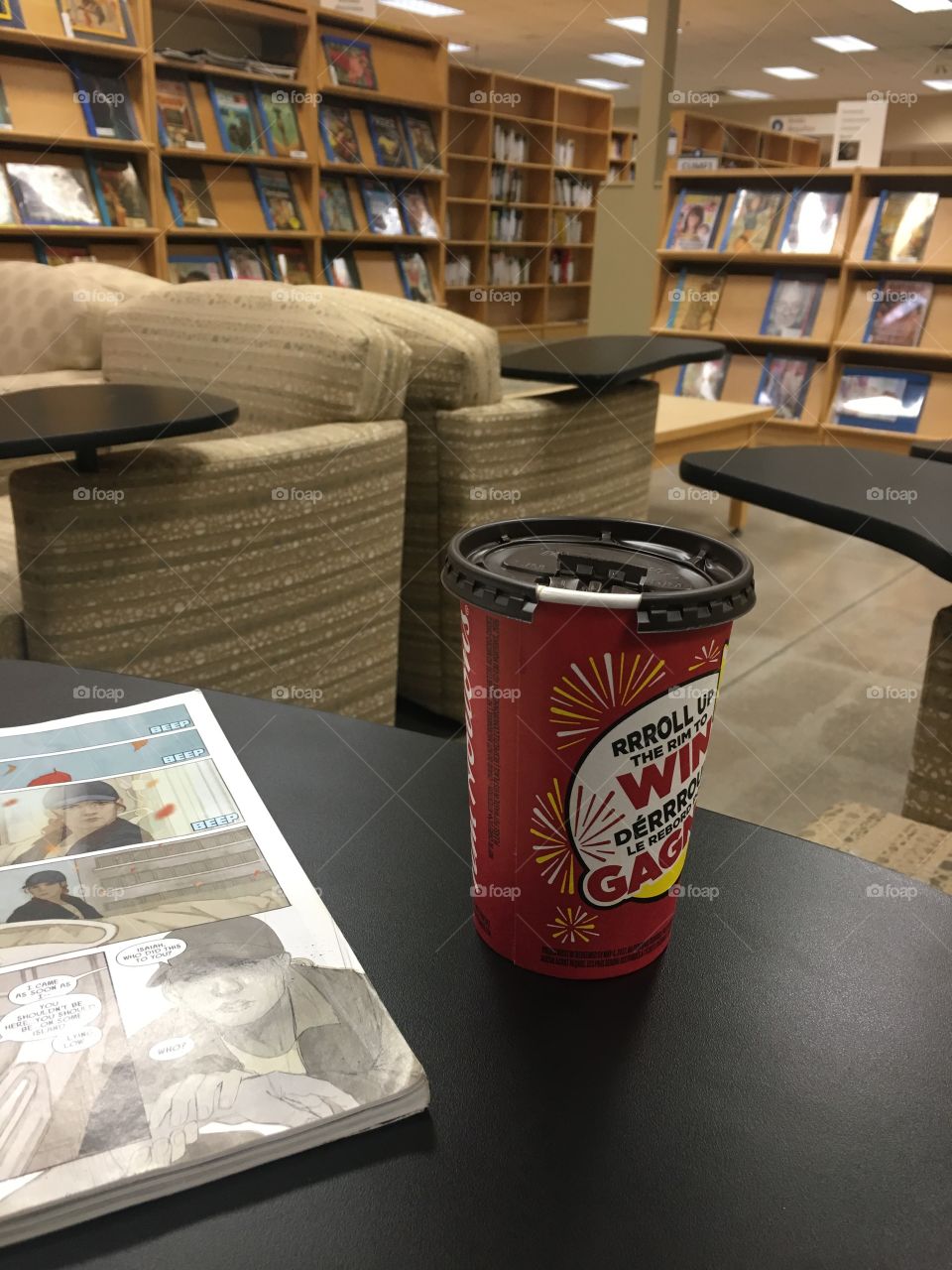 A book and a coffee sit on a table in a library.