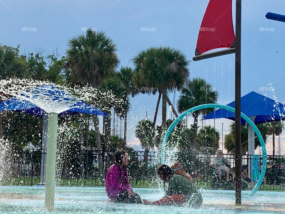 Children having lots of fun in the water at the colorful kids splash pad at the city park for children during a really warm day in Florida.