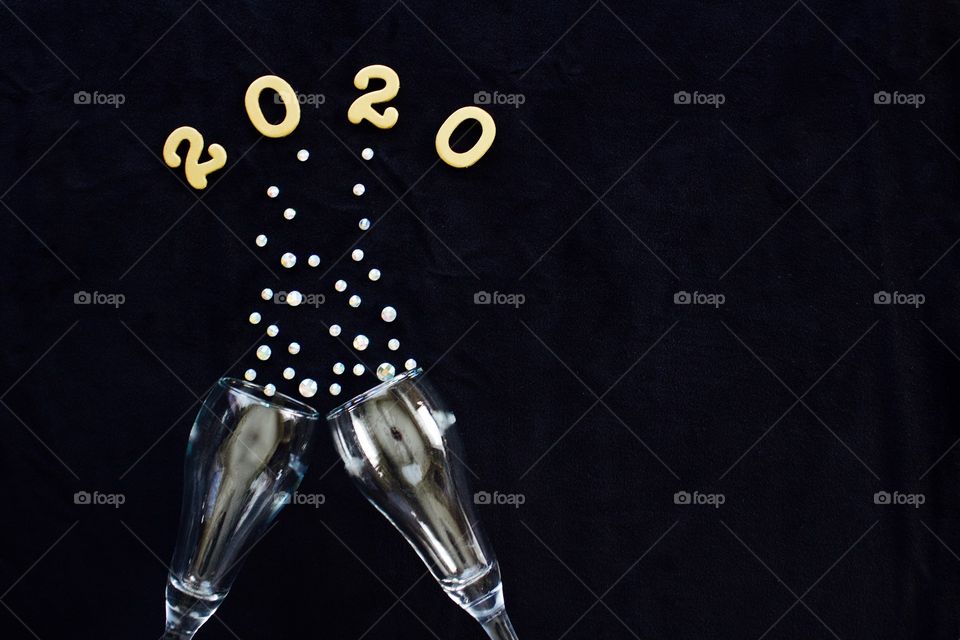 Flat lay of the numbers ‘2020’ in gold above gleaming champagne glasses with rhinestone bubbles on black background - copy space on right side of landscape format