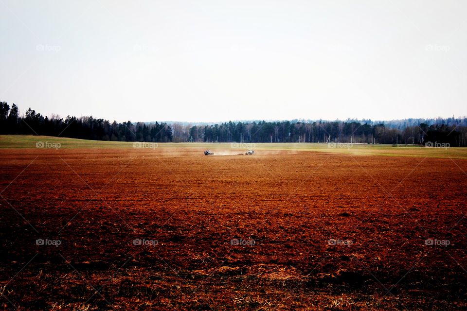Rural scene, harvesting, two tractors on a large reddish field