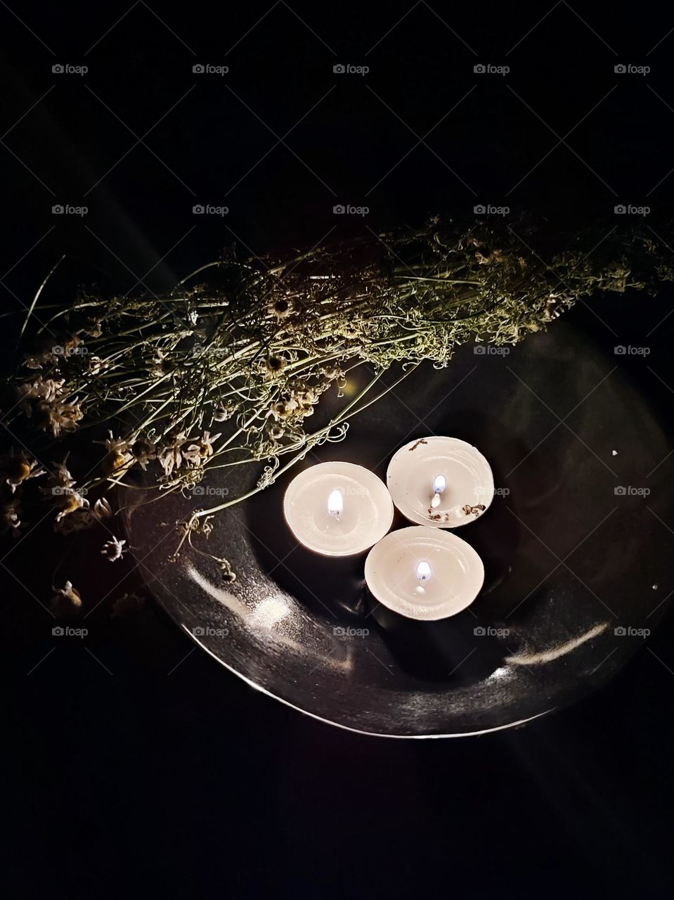 3 burning floating candles on the black background. Fire element, magical ceremony, meditation with herbal incense, bouquet of camomile